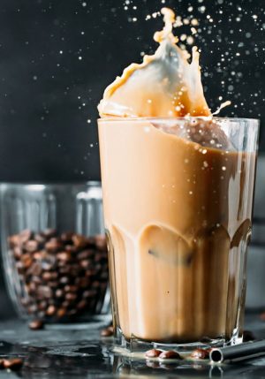 Splash of ice coffee drink on a dark background. Refreshing Iced cappuccino liquid drink pouring into a tall glass with ice cubes. Cold beverage wave. Close-up design liquor milk, coffee and ice.
